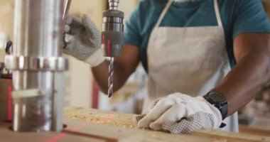 Mid section of african american male carpenter drilling wood with a laser drill in a carpentry shop. carpentry, craftsmanship and handwork concept