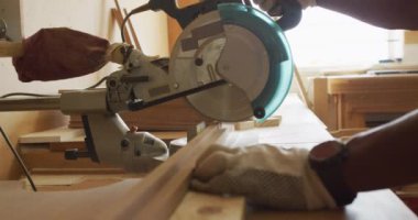 Close up of african american male carpenter hand's cutting wooden plank with electric chop saw. carpentry, craftsmanship and handwork concept