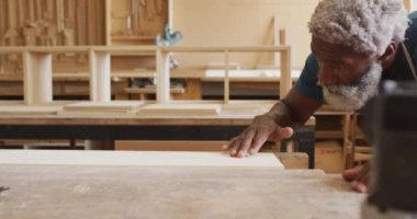 Afrikalı Amerikalı erkek marangoz bir marangozhanedeki tahtadan tozları üflüyor. Marangozluk, işçilik ve el işi konsepti