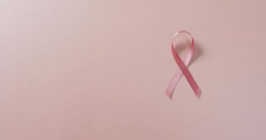 Video of pink breast cancer ribbon on pale pink background. medical awareness support campaign symbol for breast cancer.