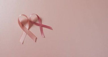 Video of two pink breast cancer ribbons on pale pink background. medical awareness support campaign symbol for breast cancer.