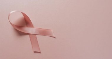 Video of pink breast cancer ribbon and shadow on pale pink background. medical awareness support campaign symbol for breast cancer.
