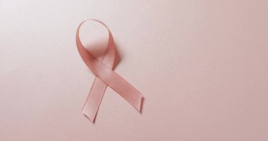 Video of pink breast cancer ribbon on pale pink background. medical awareness support campaign symbol for breast cancer.