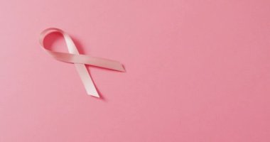 Video of pink breast cancer ribbon on pale pink background. medical awareness support campaign symbol for breast cancer.