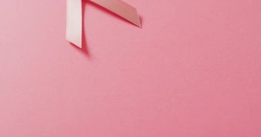Video of pink breast cancer ribbon on pale pink background. medical awareness support campaign symbol for breast cancer.