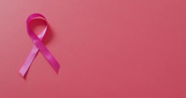 Video of pink breast cancer ribbon on dark pink background. medical awareness support campaign symbol for breast cancer.