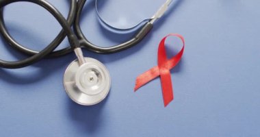 Video of stethoscope and red blood cancer ribbon on blue background. medical and healthcare awareness support campaign symbol for blood cancer.