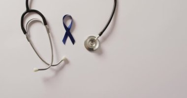 Video of stethoscope and dark blue colon cancer ribbon on white background. medical and healthcare awareness support campaign symbol for colon cancer.