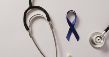 Video of stethoscope and dark blue colon cancer ribbon on pale blue background. medical and healthcare awareness support campaign symbol for colon cancer.