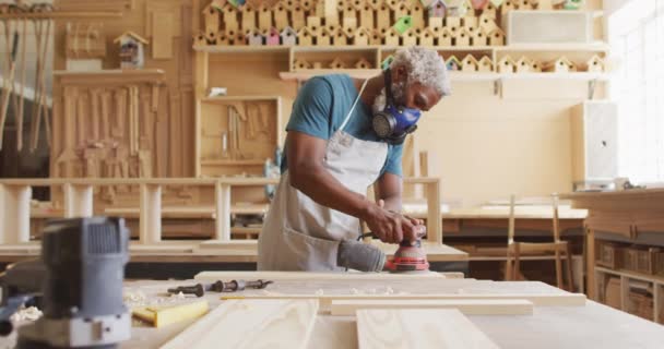 African American Male Carpenter Wearing Protective Mask Sanding Wooden Plank — Video Stock