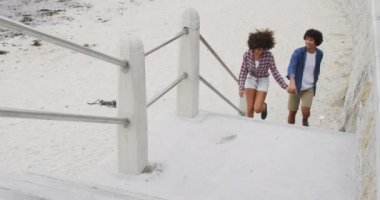 Afrika kökenli Amerikalı çift plajın yakınındaki merdivenlerden çıkarken el ele tutuşuyorlar. Aşk ve ilişki kavramı