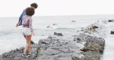 Afrika kökenli Amerikalı çift deniz kenarındaki kayalarda el ele yürüyorlar. Aşk ve ilişki kavramı