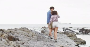 Afrika kökenli Amerikalı çift deniz kenarındaki kayalarda el ele yürüyorlar. Aşk ve ilişki kavramı