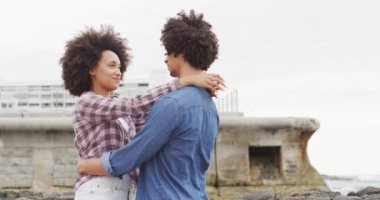 Afrika kökenli Amerikalı çift deniz kenarındaki kayalıklarda birbirini kucaklıyor. Aşk ve ilişki kavramı