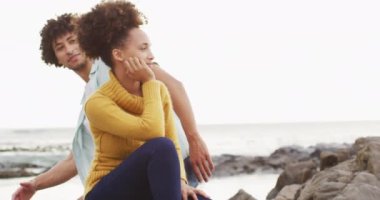 Afrika kökenli Amerikalı çift, deniz kenarındaki kayalıklarda oturup birbirlerine sarılıyorlar. Aşk ve ilişki kavramı