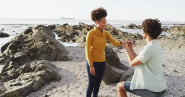 Afrika kökenli Amerikalı bir adam deniz kenarındaki kayalıklara kız arkadaşının parmağına yüzük takıyor. Aşk ve ilişki kavramı