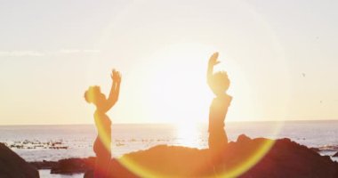 Afrika kökenli Amerikalı çift gün batımında deniz kenarındaki kayalıklarda yoga yapıyorlar. Aşk ve ilişki kavramı