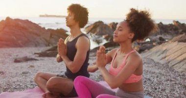 Afrika kökenli Amerikalı çift gün batımında deniz kenarındaki kayalarda yoga yapıyor ve meditasyon yapıyorlar. Aşk ve ilişki kavramı