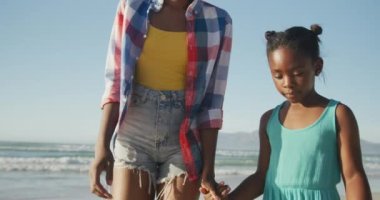 Afrika kökenli Amerikalı anne ve kızı sahilde birbirlerine sarılıyorlar. Aile seyahati ve tatil konsepti