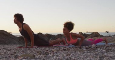 Afrika kökenli Amerikalı çift gün batımında deniz kenarındaki kayalarda yoga yapıyor. Aşk ve ilişki kavramı