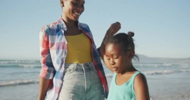 Afrika kökenli Amerikalı bir anne kızının elini tutuyor ve sahilde yürüyor. Aile seyahati ve tatil konsepti