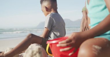 Afrikalı Amerikalı erkek ve kız kardeşler kumsalda kumla oynuyorlar. Aile seyahati ve tatil konsepti