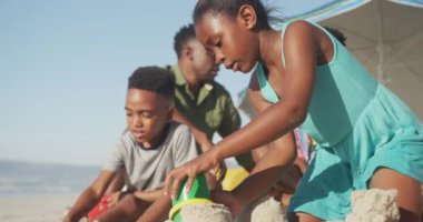 Afrikalı Amerikalı erkek ve kız kardeşler kumsalda kumla oynuyorlar. Aile seyahati ve tatil konsepti