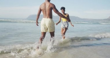 Afrika kökenli Amerikalı çift sahildeki dalgaların yanında birbirlerine sarılıyorlar. Aile seyahati ve tatil konsepti