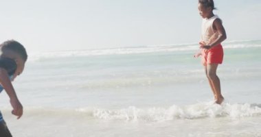 Afrika kökenli Amerikalı erkek ve kız kardeşler plajda zıplayıp eğleniyorlar. Aile seyahati ve tatil konsepti
