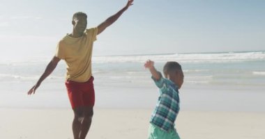 Afrika kökenli Amerikalı baba ve oğul kolları açık sahilde eğleniyorlar. Aile seyahati ve tatil konsepti