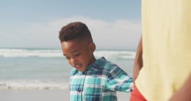Sahilde yürürken babasının elini tutan Afrikalı Amerikalı çocuk. Aile seyahati ve tatil konsepti