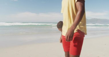 Sahilde yürürken babasının elini tutan Afrikalı Amerikalı çocuk. Aile seyahati ve tatil konsepti