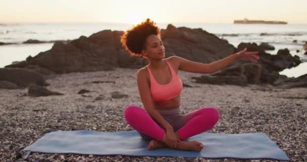 非洲裔美国妇女在日落时练习瑜伽 在海边的岩石上冥想 健康的生活方式和生活观念 — 图库视频影像