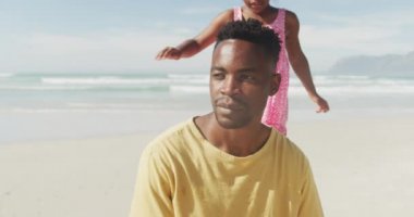 Afrikalı Amerikalı kız, plajda babasına arkadan sarılıyor. Aile seyahati ve tatil konsepti