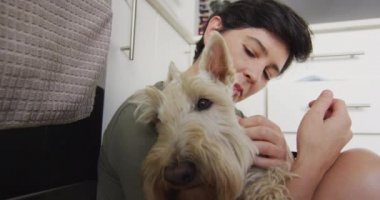 Evdeki mutfakta oturan beyaz bir kadın köpeğini öpüyor. evcil hayvan sevgisi ve bakım kavramı