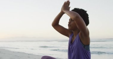 Afrika kökenli Amerikalı kadın güneşli sahilde yoga ve meditasyon yapıyor. sağlıklı ve aktif zaman plaj tatili.