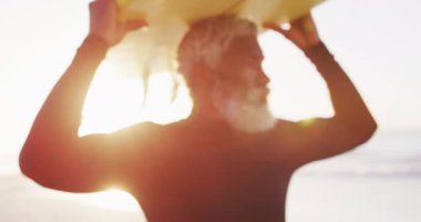 Kıdemli Afro-Amerikan adam güneşli sahilde sörf tahtasıyla yürüyor. sağlıklı ve aktif zaman plaj tatili.