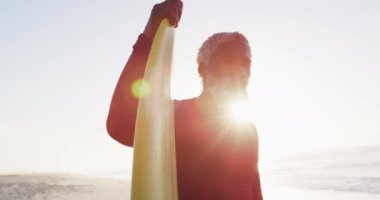 Kıdemli Afro-Amerikan adam güneşli sahilde sörf tahtası tutuyor. sağlıklı ve aktif zaman plaj tatili.