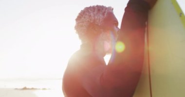 Kıdemli Afro-Amerikan adam güneşli sahilde sörf tahtası tutuyor. sağlıklı ve aktif zaman plaj tatili.