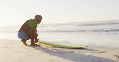 Kıdemli Afro-Amerikan adam güneşli sahilde sörf yapmadan önce hazırlanıyor. sağlıklı ve aktif zaman plaj tatili.