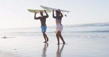 Mutlu Afro-Amerikan çifti güneşli sahilde sörf tahtasıyla yürüyor. sağlıklı ve aktif zaman plaj tatili.