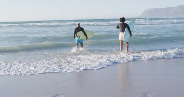 快乐的非洲裔美国夫妇在阳光灿烂的海滩上与冲浪板赛跑 健康而活跃的海滨假期 — 图库视频影像