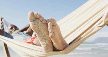 Mutlu kıdemli Afrikalı Amerikalı adam güneşli sahilde hamakta yatıyor. sağlıklı ve aktif zaman plaj tatili.