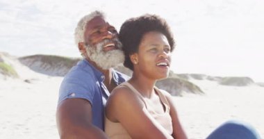 Mutlu Afro-Amerikan çifti güneşli sahilde oturup kucaklaşıyor. sağlıklı ve aktif zaman plaj tatili.