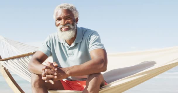 晴れたビーチでハンモックに座って幸せなシニアアフリカ系アメリカ人の男性の肖像画 健康的で活発な時間のビーチホリデー — ストック動画