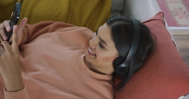 Video Happy Biracial Woman Lying Sofa Headphones Using Smartphone Leisure Royalty Free Stock Footage