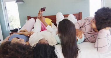 Yatakta uzanan ve yatak odasında akıllı telefon kullanan mutlu bayan arkadaşlar. evde kaliteli zaman geçirmek.