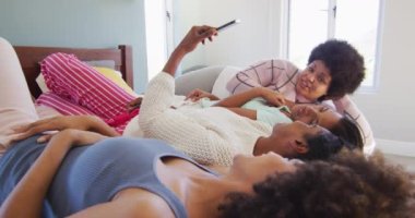 Yatakta uzanan ve yatak odasında akıllı telefon kullanan mutlu bayan arkadaşlar. evde kaliteli zaman geçirmek.