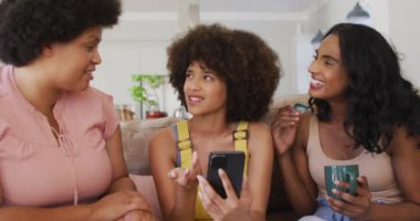 Oturma odasındaki kanepede oturan, konuşan ve gülümseyen çeşitli bayan arkadaşlar. evde kaliteli zaman geçirmek.