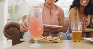 Oturma odasındaki kanepede oturup pizza yiyen çeşitli bayan arkadaşlar. evde kaliteli zaman geçirmek.